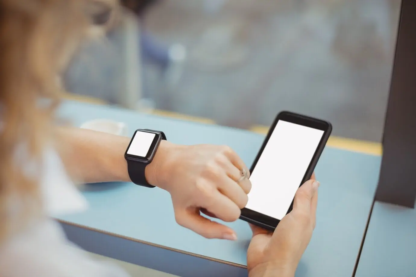 Woman using her mobile phone and checking the time at a counter.