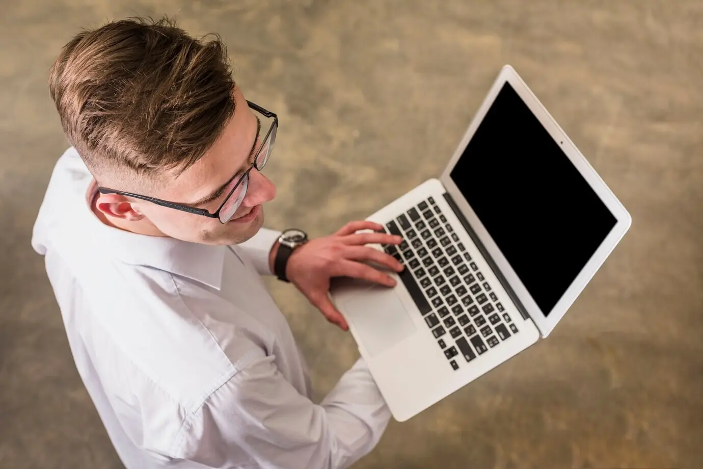 Top-down view of a young man using a laptop, holding it in his hand.