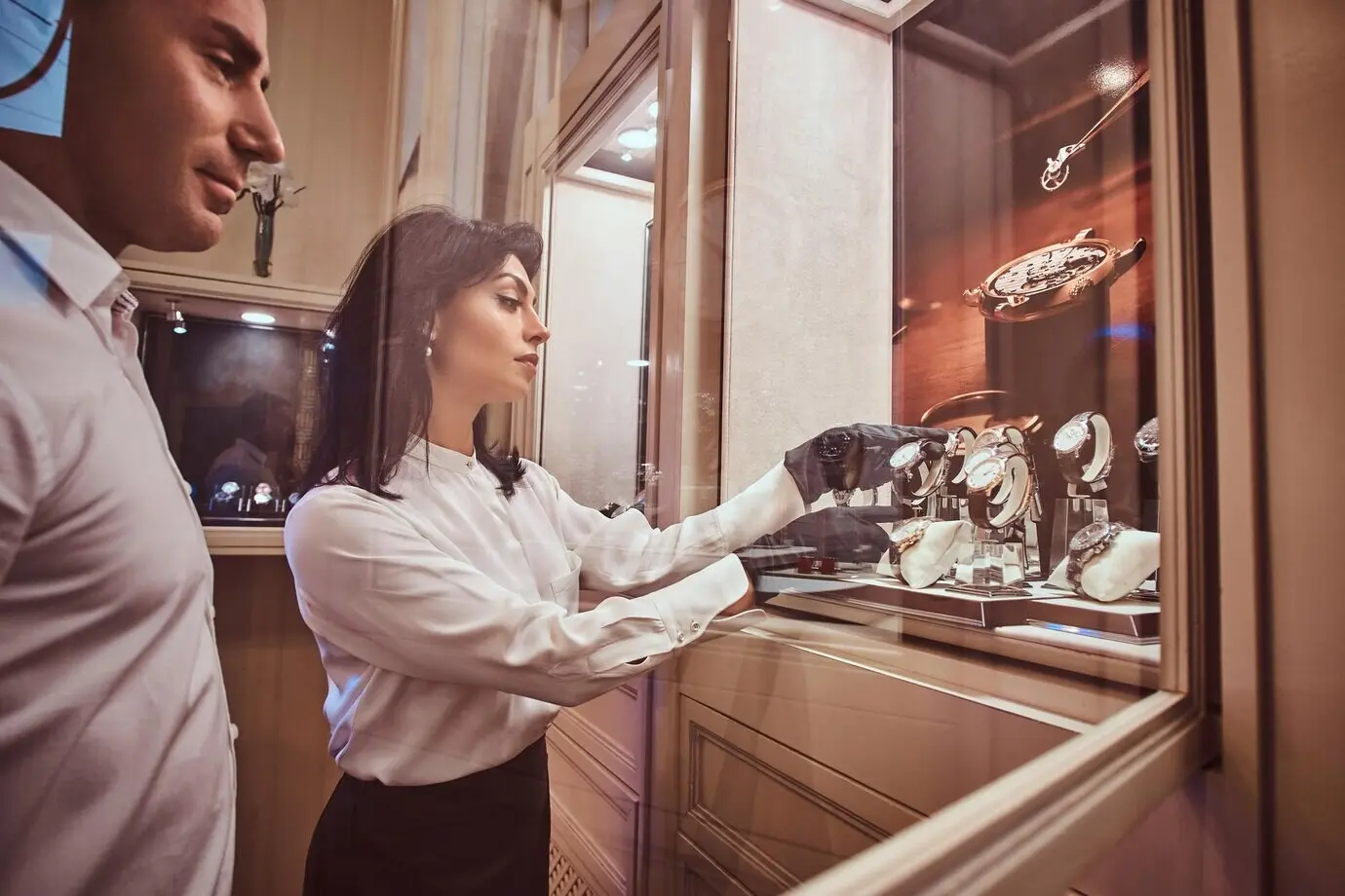 In the luxury jewelry store, the seller shows the client an exclusive men's watch while standing next to an open showcase.