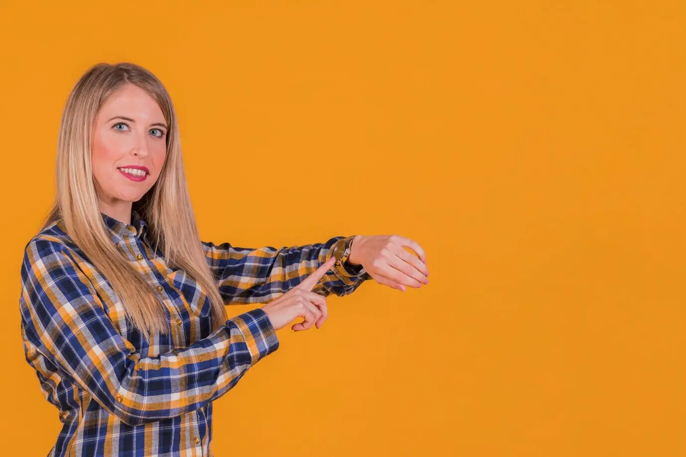 A portrait showing a young woman checking the time on her wristwatch in front of an orange background.